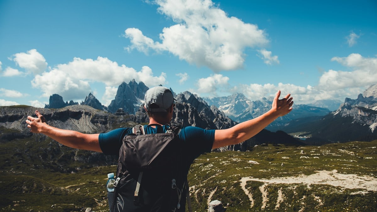 man in black t-shirt and black backpack standing on mountain under blue sky and white